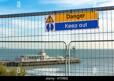 Gefahr fernzuhalten Zeichen auf Draht-Barriere am East Cliff nach Erdrutsch mit Bournemouth Pier im Hintergrund, Bournemouth, Dorset im November Stockfoto
