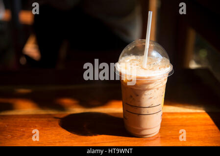 Kalter Kaffee im Plastikbecher auf braunen Holztisch im Café. Stockfoto