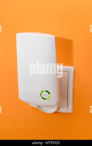 WLAN Repeater in die Steckdose auf orange Wand. Einfach weg, drahtloses Netzwerk im Haus zu verlängern Stockfoto