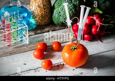 Drei Spritzen in der Tomate. Gentechnisch veränderte Lebensmittel Konzept auf hölzernen Hintergrund. Stockfoto