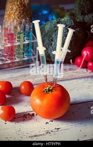 Drei Spritzen in der Tomate. Gentechnisch veränderte Lebensmittel Konzept auf hölzernen Hintergrund. Stockfoto