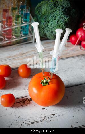 Drei Spritzen in der Tomate. Gentechnisch veränderte Lebensmittel Konzept auf hölzernen Hintergrund. Stockfoto