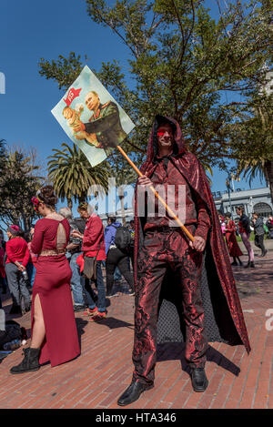 San Francisco, USA. 8. März 2017.  Ein Mann, gekleidet in allen roten Brokat mit glitzernden Umhang hält ein Schild mit einem Bild von Putin hält ein "Baby Trump" an der San Francisco International Women-Tages-Rallye am Justin Herman Plaza. Viele Demonstranten trugen rote um Unterstützung für den "Tag ohne eine Frau" Streik zu zeigen. Bildnachweis: Shelly Rivoli/Alamy Live-Nachrichten Stockfoto