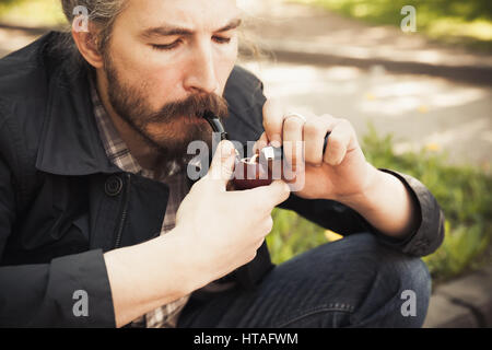 Junge asiatische bärtiger Mann Rauchen einer Pfeife im Sommerpark, close-up Portrait mit selektiven Fokus Stockfoto