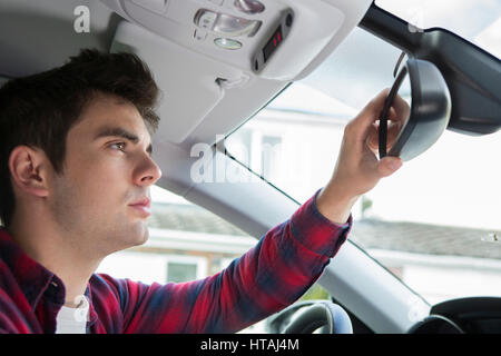 Junge männliche Fahrer im Auto Rückspiegel prüfen Stockfoto