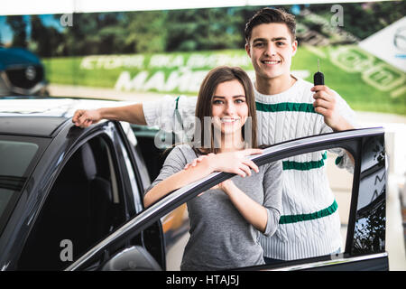 Schöne junge Paar lächelt und Blick in die Kamera und stützte sich auf ihr neues Auto in einem motor Show. Stockfoto