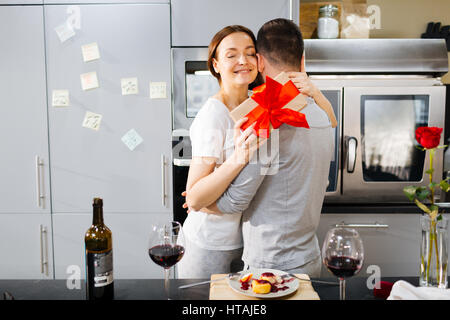 Junge Frau mit Gegenwart umarmen ihr Mann in der Küche beim romantischen Frühstück Stockfoto