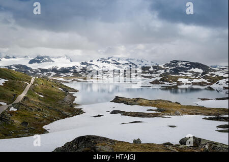 Wunderschöne norwegische Landschaft mit hohen Bergplateau, See, Schnee und Straße in den Felsen. Kreisstraße 55, Sognefjellet, Norwegen. Stockfoto