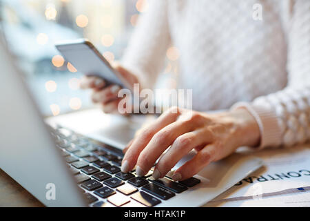 Nahaufnahme von unkenntlich beschäftigte Frau Multitasking: Smartphone in der hand halten und schreiben Nachricht während der Arbeit mit Laptop und Dokumentation im Café Stockfoto
