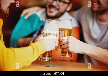 Closeup Aufnahme von drei Männern Klirren klassische hohe Gläser mit schaumigen Lagerbier, genießen Sie ihre Tagung im Irish Pub Stockfoto