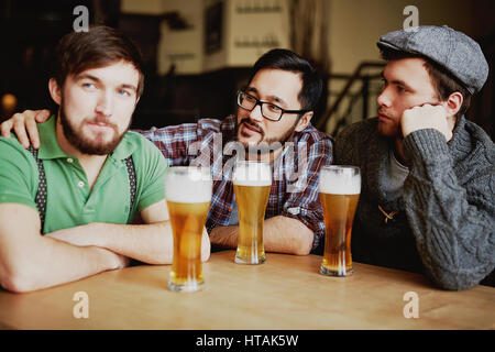 Oldschool Herren get together im Pub: drei Männer sitzen am Tisch mit hohen Gläsern der schaumigen frisch gebraut Handwerk Bier genießen Sie ihre Tagung Stockfoto