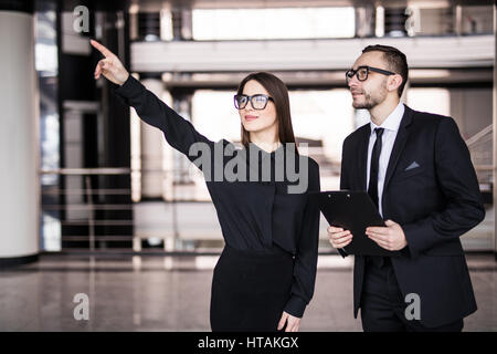 Junge Geschäftsfrau zeigt etwas Geschäftsmann durch Glas gesehen Stockfoto