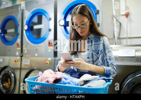 Junge Frau mit Handy während des Wartens auf ihr wiederum in Wäscherei Stockfoto
