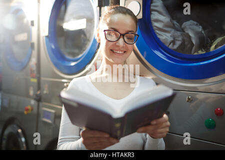 Smiley Student Lesebuch während des Wartens auf Kleidung gewaschen werden Stockfoto