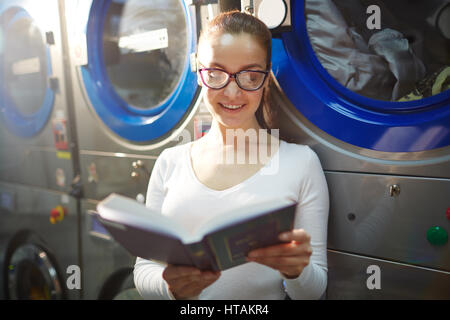 Hübsche junge Frau liest in der Wäscherei Stockfoto