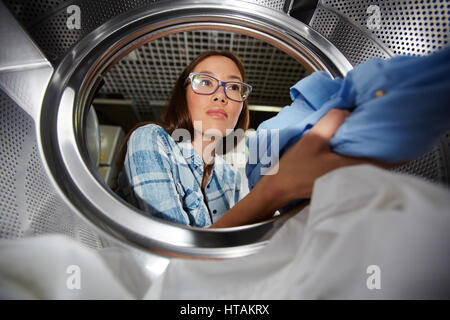 Junge Frau mit Kleidung im Trockner Tür Stockfoto