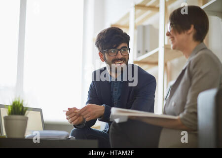 Moderne orientalische Mann trägt kreative Frisur und Brille, die Kommunikation mit seinen Kollegen im modernen Büro, beide lächelnd suchen glücklich Stockfoto
