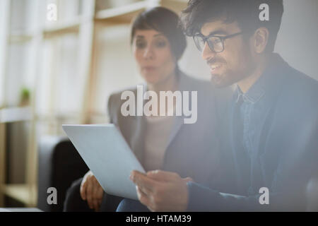 Junge hübsche mittleren östlichen Geschäftsmann, tragen, kreative Frisur und Brille während der Laptop-Bildschirm betrachten und diskutieren mit Coll lächelnd Stockfoto