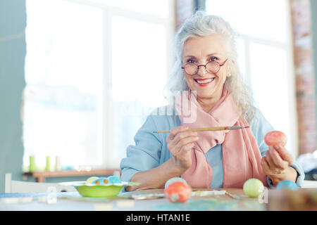 Grauhaarige Frau bemalen von Ostereiern Stockfoto
