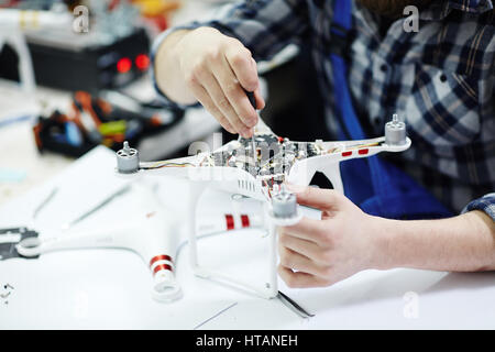 Closeup Schuss von männlichen Händen öffnen Quadrocopter Drohne und Abschrauben der Hauptplatine auf weißen Tisch in Werkstatt arbeiten Stockfoto