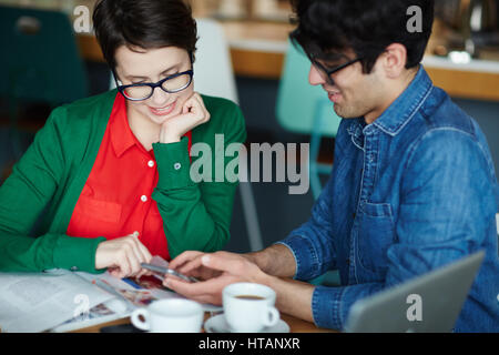 Porträt von zwei jungen kreativen gekleidet im Business casual lächelnden Blick auf Smartphone während der Sitzung am Tisch im café Stockfoto