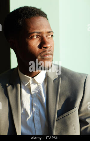 Business Portrait der schönen jungen afro-amerikanischen Mann stehend in der Sonne an Wand und wegsehen Stockfoto