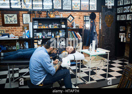 Kreative junge Mann Zeichnung Tattoo am Arm des Clients Stockfoto