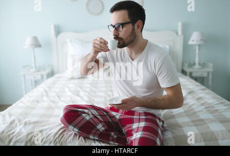 Mann im Pyjama genießen Kaffee am Morgen im Schlafzimmer Stockfoto