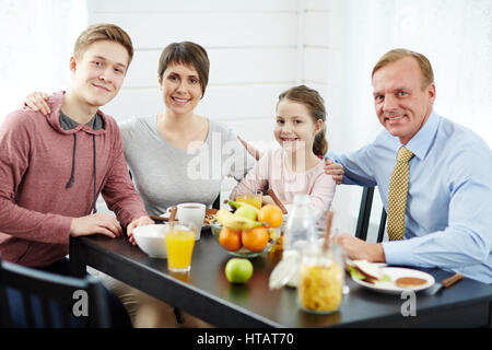 Fröhliche Eltern und Kinder sitzen um den Tisch in der Küche Stockfoto