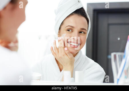 Perfekte junge Frau Anwendung Gesichtscreme im Badezimmer Stockfoto