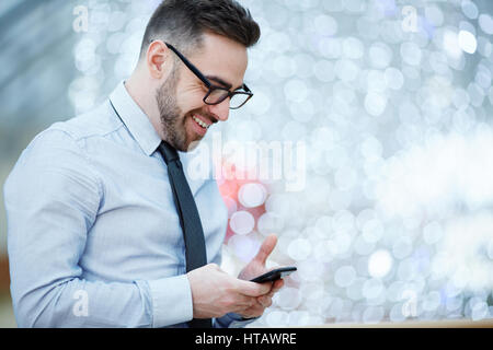 Seite Ansicht Porträt der moderne Geschäftsmann tragen Brille, Hemd und Krawatte freudig lächelnd, während lesen SMS von Smartphone gegen der unscharf Stockfoto