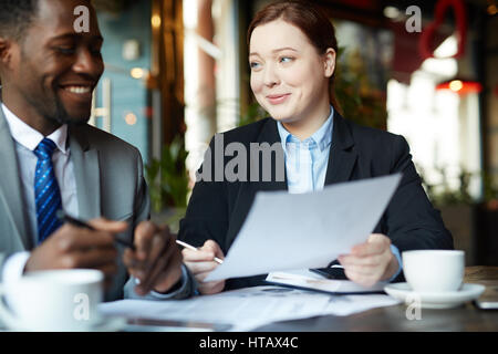 Porträt von zwei Geschäftsleuten treffen im modernen Café: junge berufstätige Frau lächelnd beiläufig während der Arbeit, afrikanisch-amerikanischer Partner zu erklären, eine Stockfoto