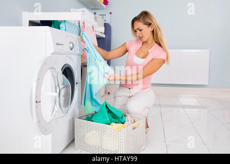 Junge Frau Blick auf Kleidung nach dem Waschen In der Waschmaschine im Hauswirtschaftsraum Stockfoto