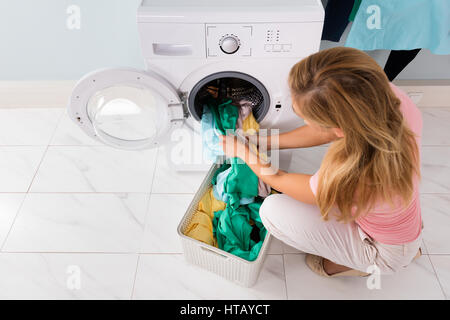 High Angle View Of Frau laden Kleidung aus Korb In Waschmaschine im Hauswirtschaftsraum Stockfoto