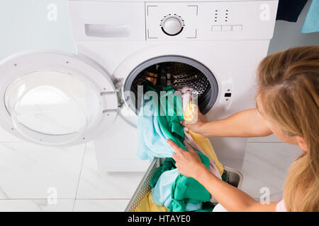 High Angle View Of Frau laden Kleidung aus Korb In Waschmaschine im Hauswirtschaftsraum Stockfoto