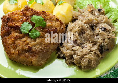 Gebratenes Schweinefleisch Schnitzel serviert mit gekochten Kartoffeln und gebratene Sauerkraut auf einem Teller Stockfoto