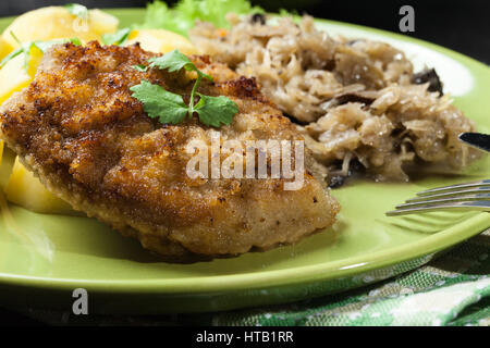 Gebratenes Schweinefleisch Schnitzel serviert mit gekochten Kartoffeln und gebratene Sauerkraut auf einem Teller Stockfoto