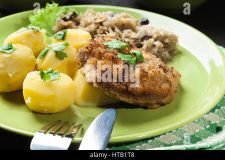 Gebratenes Schweinefleisch Schnitzel serviert mit gekochten Kartoffeln und gebratene Sauerkraut auf einem Teller Stockfoto