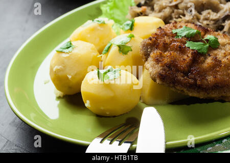 Gekochte Kartoffeln mit gebratenem Schweinefleisch Schnitzel und gebratenes Sauerkraut auf einem Teller Stockfoto