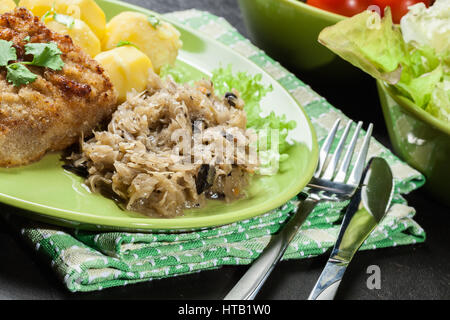 Gebratenes Sauerkraut mit gebratenem Schweinefleisch Schnitzel und Kartoffeln auf einem Teller Stockfoto