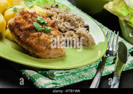 Gebratenes Schweinefleisch Schnitzel serviert mit gekochten Kartoffeln und gebratene Sauerkraut auf einem Teller Stockfoto