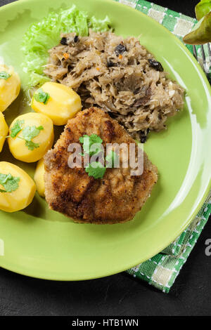 Gebratenes Schweinefleisch Schnitzel serviert mit gekochten Kartoffeln und gebratene Sauerkraut auf einem Teller Stockfoto