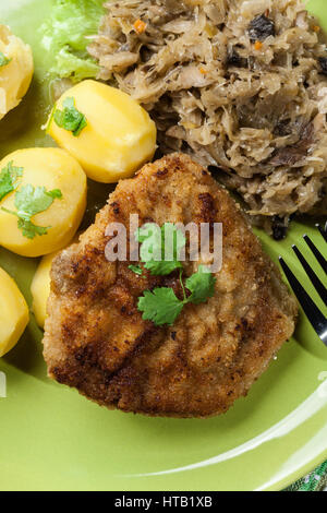 Gebratenes Schweinefleisch Schnitzel serviert mit gekochten Kartoffeln und gebratene Sauerkraut auf einem Teller Stockfoto