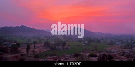 Momente vor dem Sonnenaufgang von einem Berg in Sanapur, in der Nähe von Hampi, mit Blick auf Reis-Plantagen und Berge in der Ferne. Stockfoto