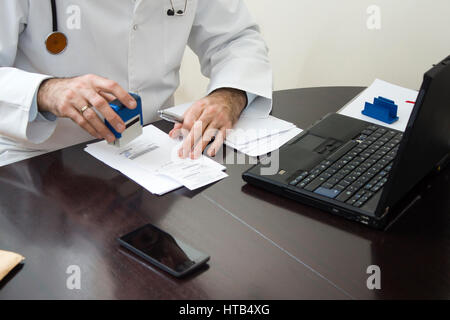 Des Arztes Hand gestempelt auf dem Rezept. Der Arzt schreibt ein Rezept an seinem Schreibtisch. Stockfoto