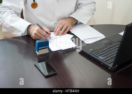 Des Arztes Hand gestempelt auf dem Rezept. Der Arzt schreibt ein Rezept an seinem Schreibtisch. Stockfoto