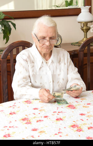 Pension. Alte Frau zählt das Geld. Alte Frau mit einem traurigen Gesicht zählt Geld beim Sitzen am Tisch. Stockfoto