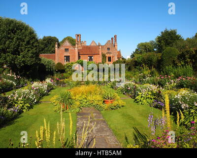 Chenies Herrenhaus mit Blick auf die bunten versunkene Garten im Juli in voller Sonne mit strahlend blauem Himmel, rosa Dahlien, Hosta, Ziergräser und Laub. Stockfoto