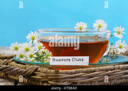 Buenos Dias (guten Morgen in Spanisch) mit Tasse Kamillentee auf blauem Hintergrund Stockfoto