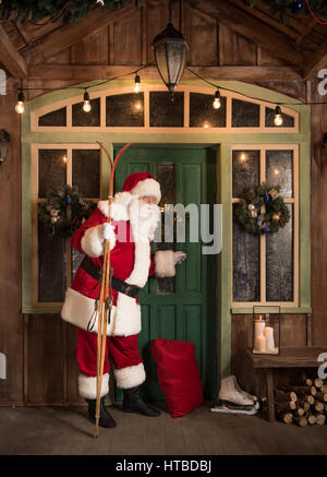 Weihnachtsmann stehend mit Skiern und klopfen in Tür Stockfoto